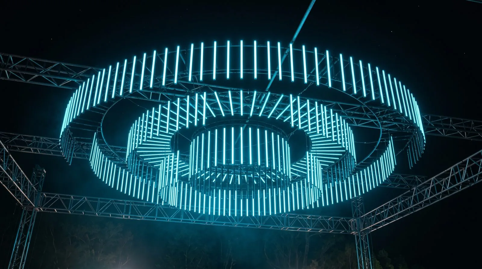 Custom PILEDS RGB pixel-bar installation forming a suspended circular ring of cyan-blue light on stage truss